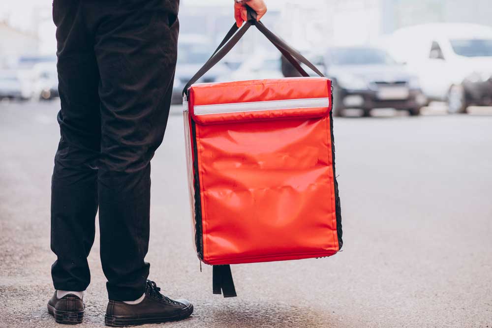 Delivery person holding a thermal transport bag for delivering perishable food products, illustrating the use of custom professional bags for maintaining the cold chain.